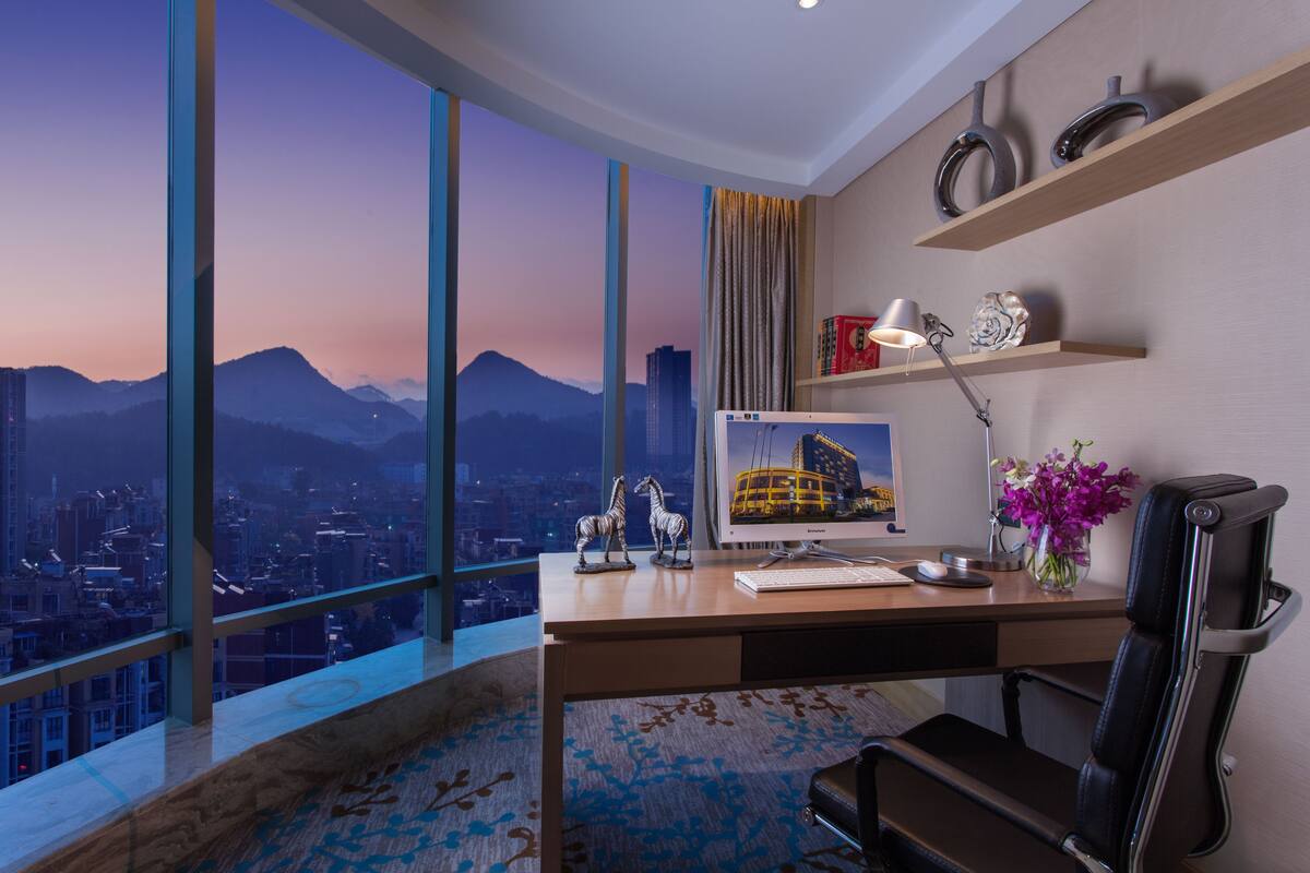 Un bureau moderne doté d’un grand bureau, d’un ordinateur et d’une chaise, offrant une vue sur le paysage urbain et les montagnes.