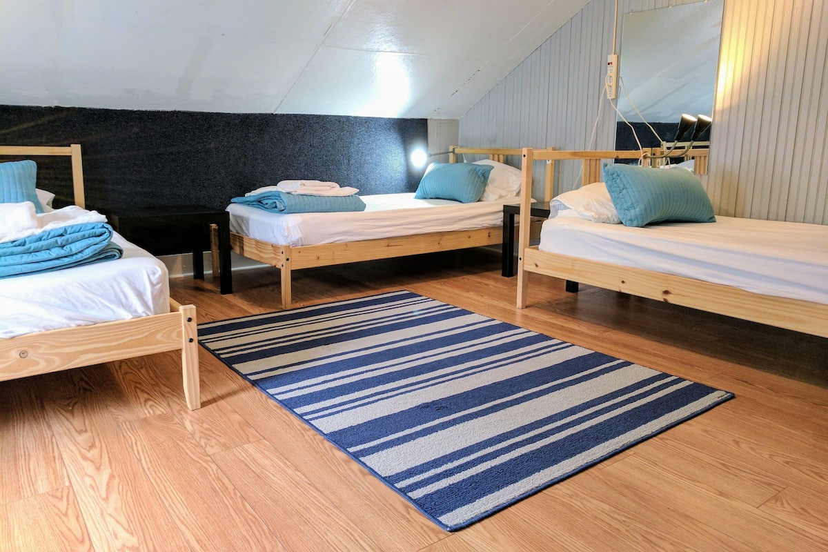 A room with three wooden beds, a blue striped rug, and a mirror on the wall.