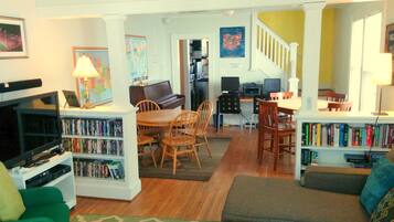 A living room with a green sofa, a dining area with a piano, and a bookshelf filled with books.