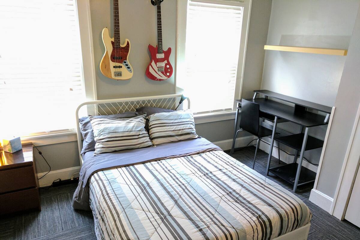 A bedroom with a bed, pillows, a desk, and two guitars on the wall.