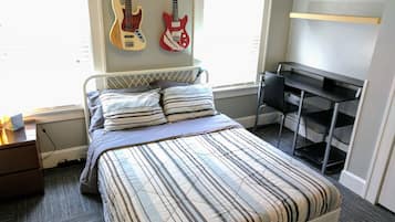 Una camera da letto con un letto, cuscini, una scrivania e due chitarre appese al muro.