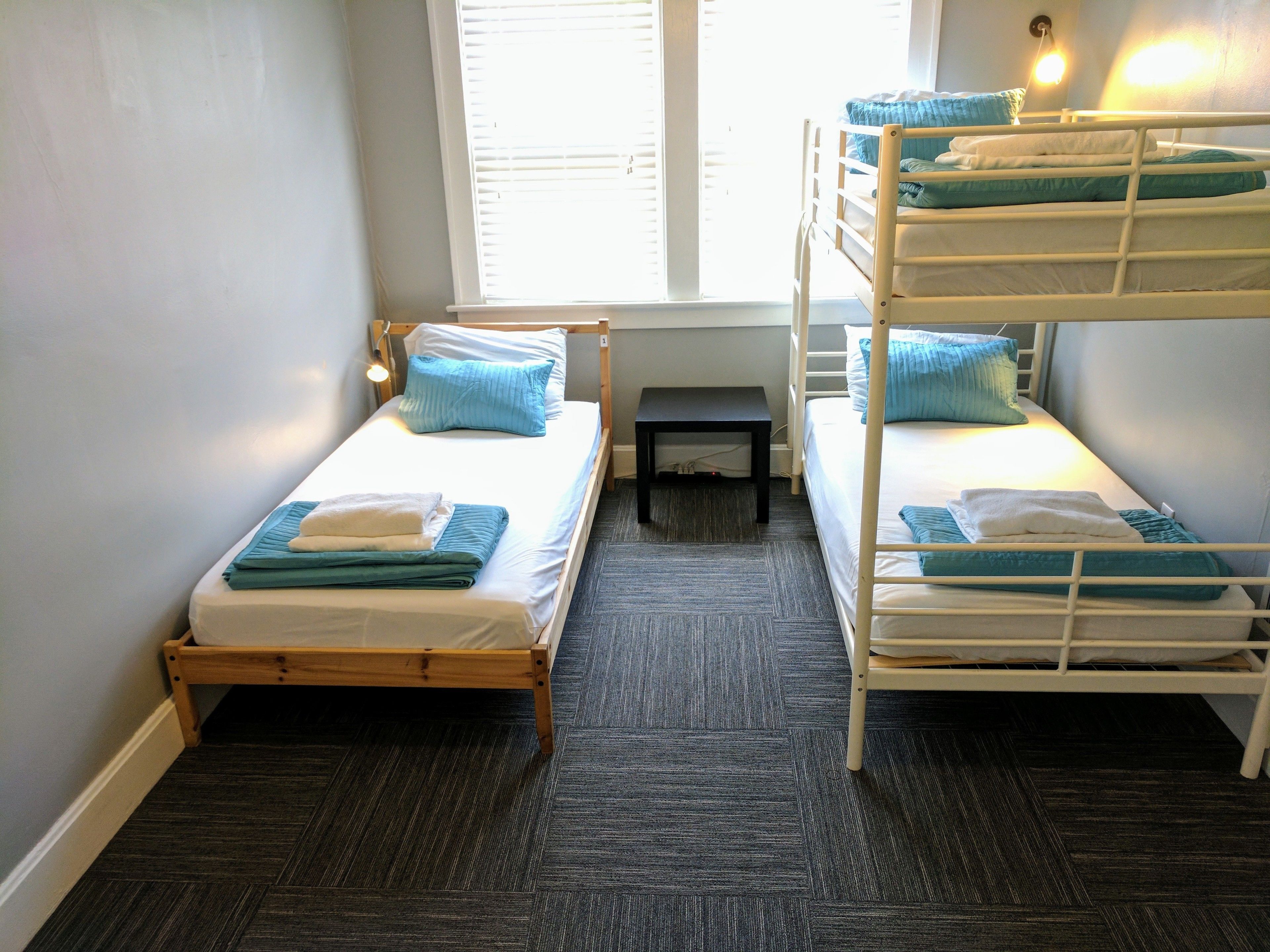 A room with two bunk beds, a small table, and a window with blinds.