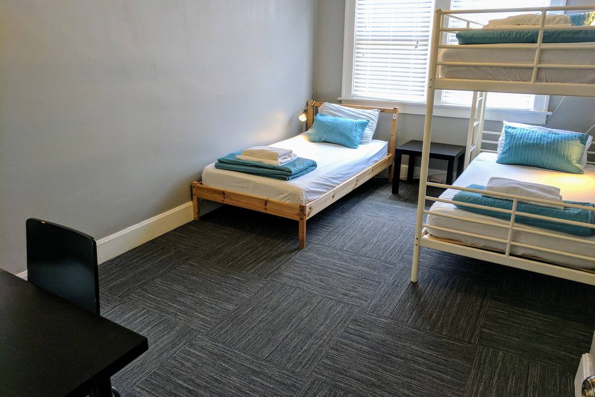 A small, neatly arranged room with a single bed, a bunk bed, and a desk.