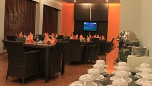 A restaurant with multiple tables set for dining, a television mounted on the wall, and a coffee machine in the background. - Hotel Griya Asri (Mataram)