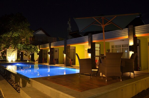 A nighttime view of a pool area with lounge chairs and a covered seating area.