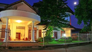 A traditional building with a covered porch, a fenced garden, and a large tree in front. - Hotel Griya Asri (Mataram)