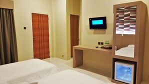 A hotel room with two beds, a desk with a flat-screen TV, a minibar, and a wardrobe. - Hotel Griya Asri (Mataram)