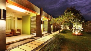 A modern building with a well-lit entrance, a pathway leading to the door, and a small tree in the foreground. - Hotel Griya Asri (Mataram)