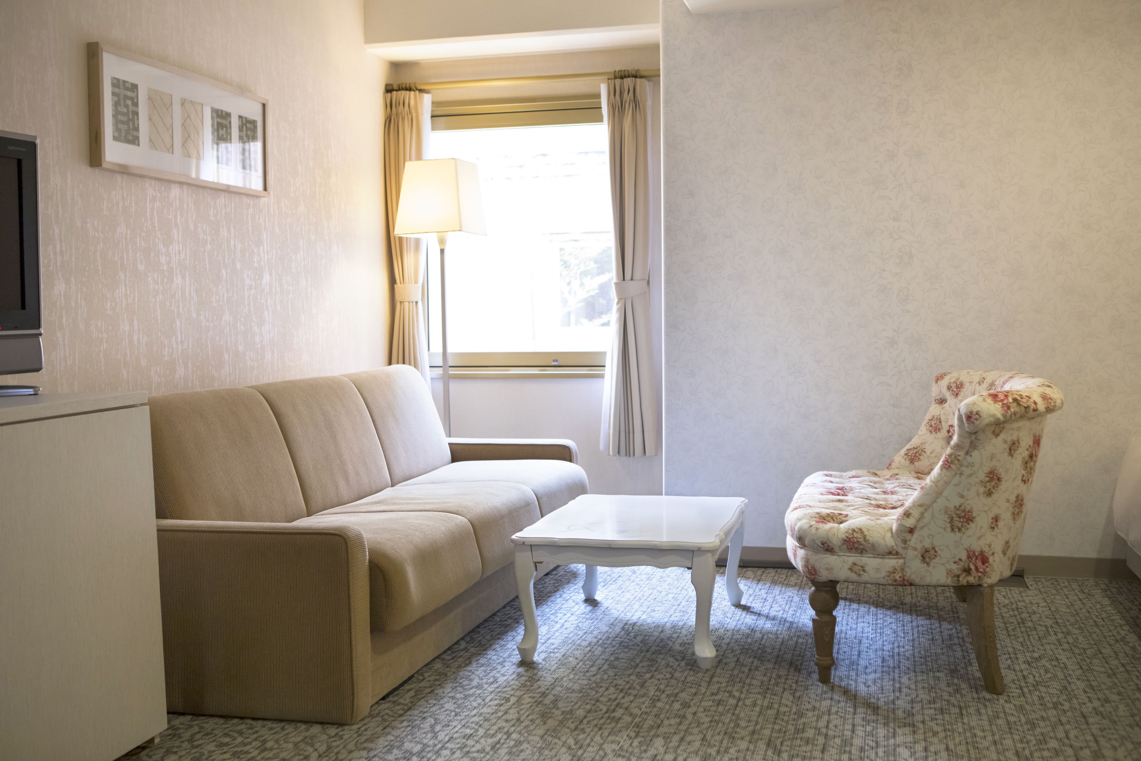 Une petite pièce, bien rangée, avec un canapé, un fauteuil, une petite table, une lampe et un téléviseur.