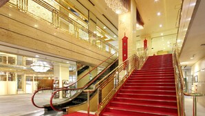 A grand staircase with red carpet and golden railings, leading to an upper floor with a glass railing and a decorative chandelier. - Nara Royal Hotel (Nara)