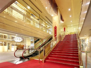 A grand staircase with red carpet and golden railings, leading to an upper floor with a glass railing and a decorative chandelier. - Nara Royal Hotel (Nara)