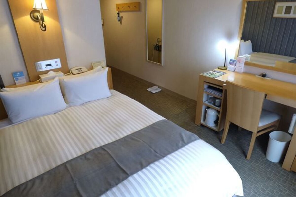 Une chambre d’hôtel comprenant un lit, une table de chevet, une lampe, un miroir et un bureau avec une chaise.