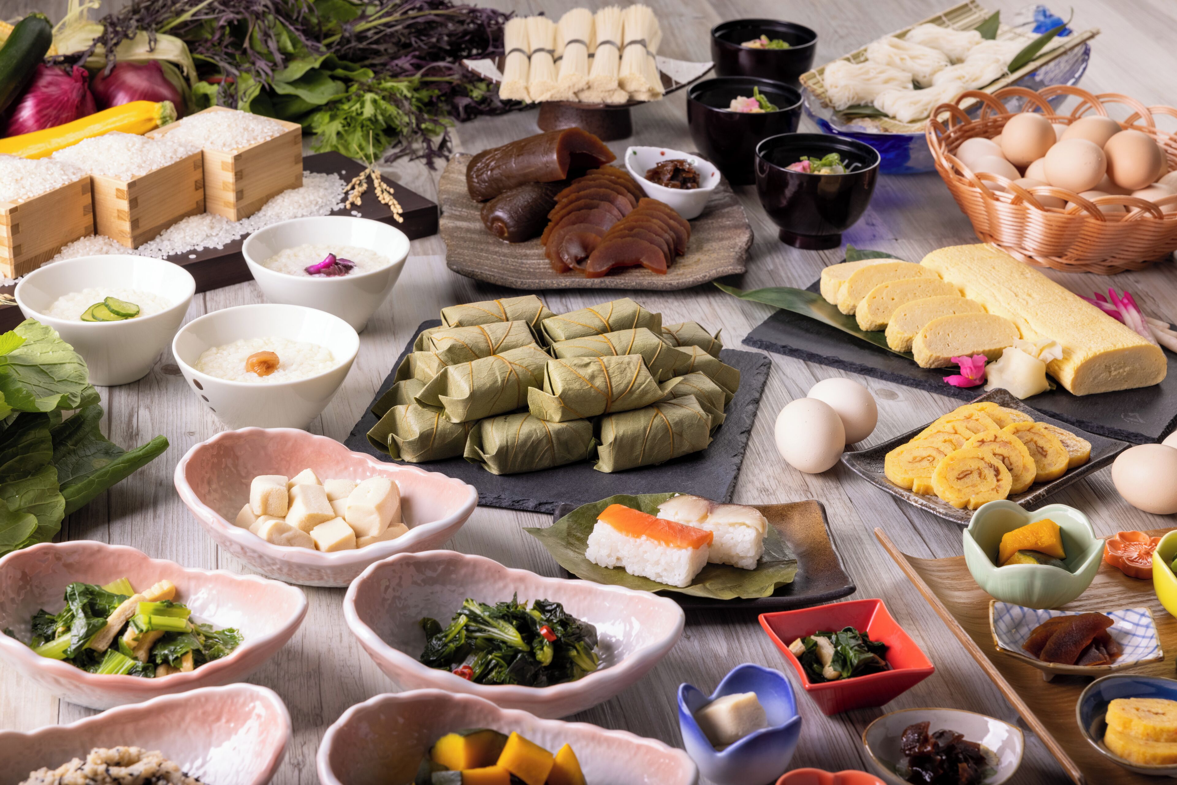 A variety of food items and dishes, including rice, vegetables, and possibly some meat, arranged on a wooden table.