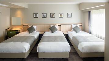 A hotel room with three single beds, a desk with a chair, a large mirror, and a wall with five framed pictures.