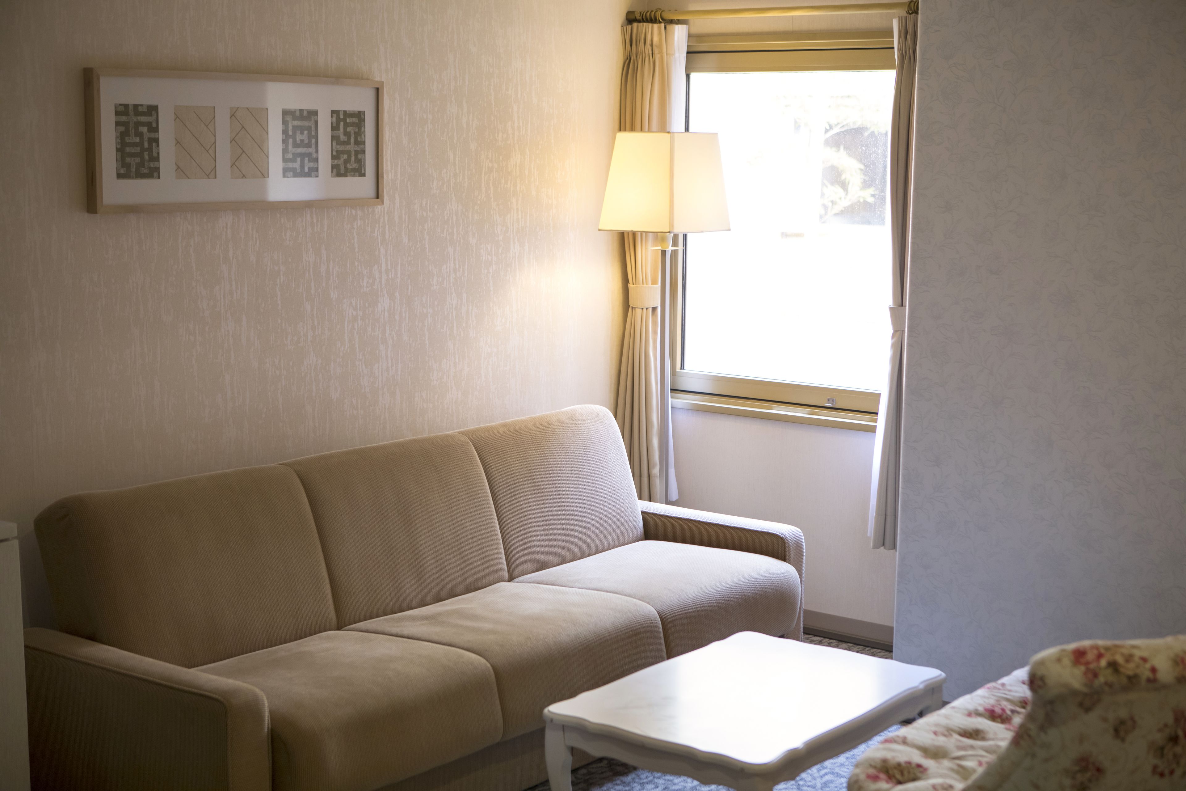 Una habitación con un sofá color beige, una mesita de centro blanca y un ventanal con cortinas.