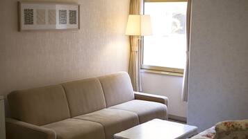 Una habitación con un sofá color beige, una mesita de centro blanca y un ventanal con cortinas.