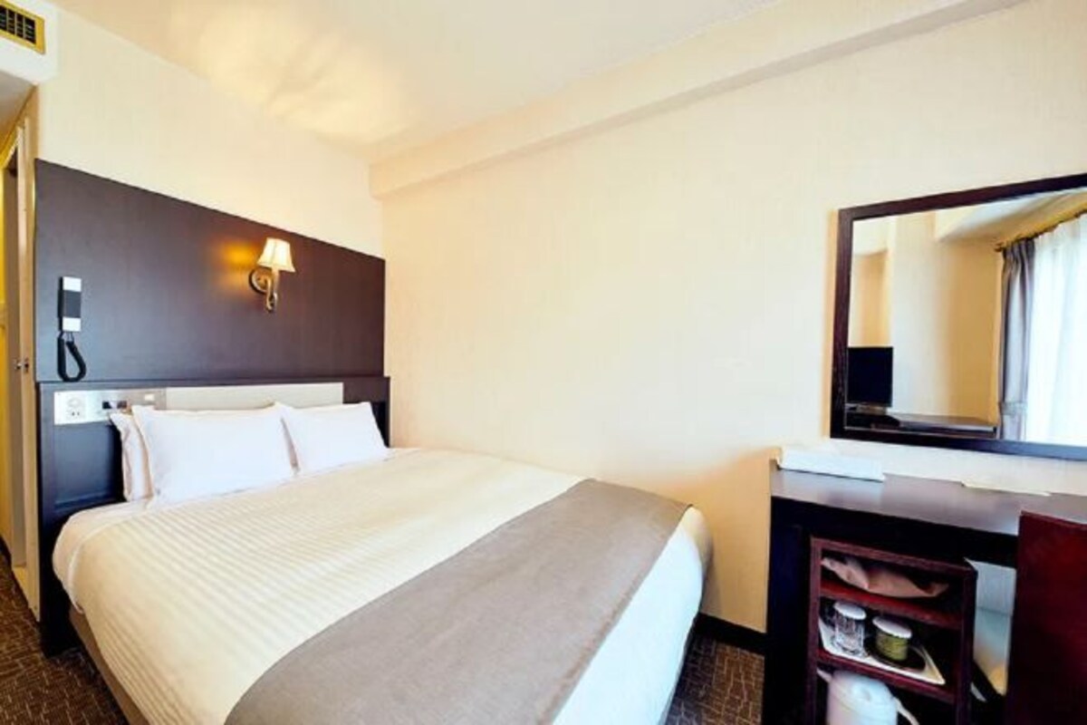 A hotel room with a large bed, a bedside table, a lamp, and a mirror.