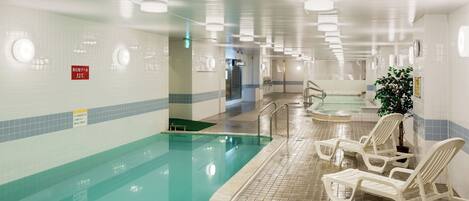 An indoor swimming pool with clear water, tiled walls, and lounge chairs along the poolside.