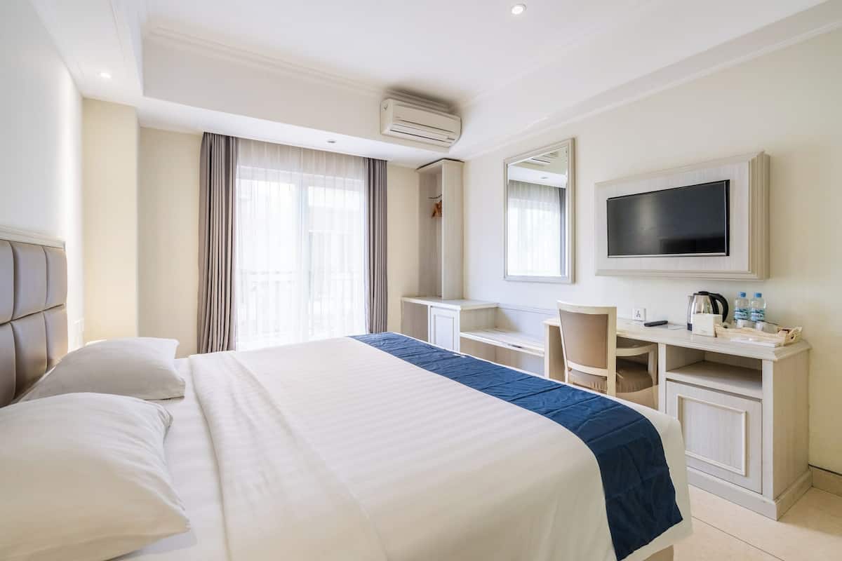 A hotel room with a large bed, a desk, a chair, a television, and a wardrobe.