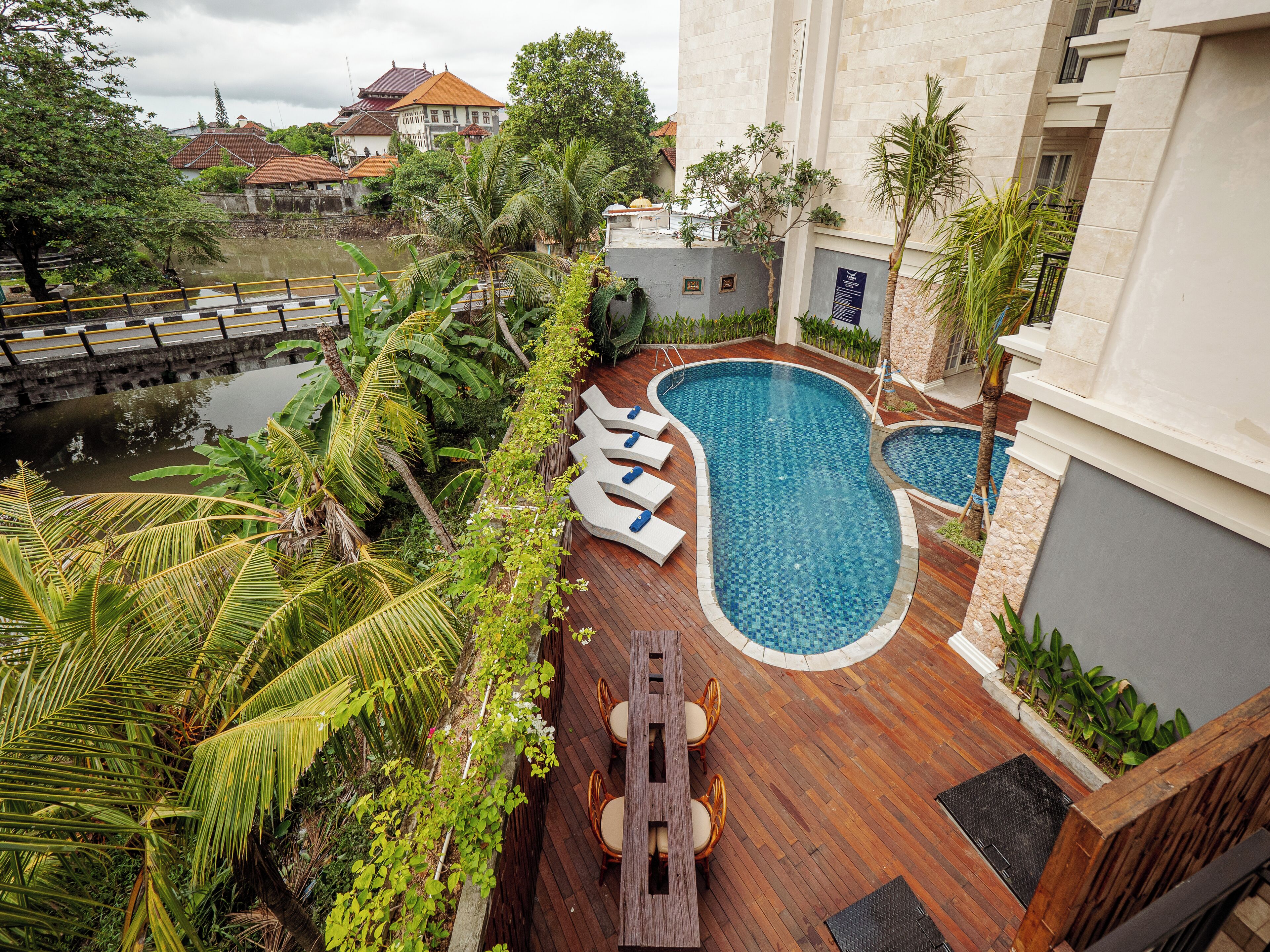 A rooftop pool with lounge chairs, surrounded by lush greenery and a view of traditional buildings.