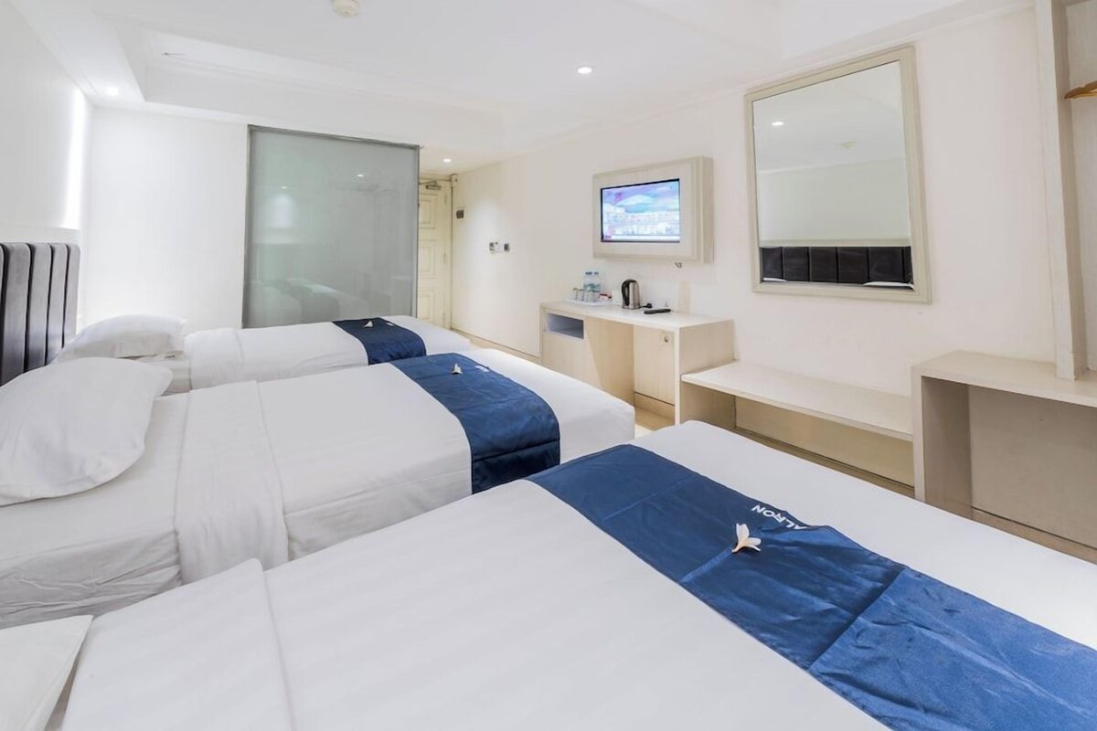 A hotel room with two beds, a desk, a television, and a mirror.