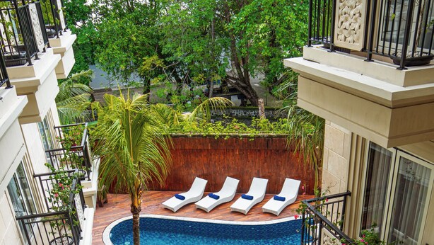 A rooftop swimming pool with lounge chairs and a palm tree. - Alron Hotel Kuta Powered by Archipelago (Kuta)