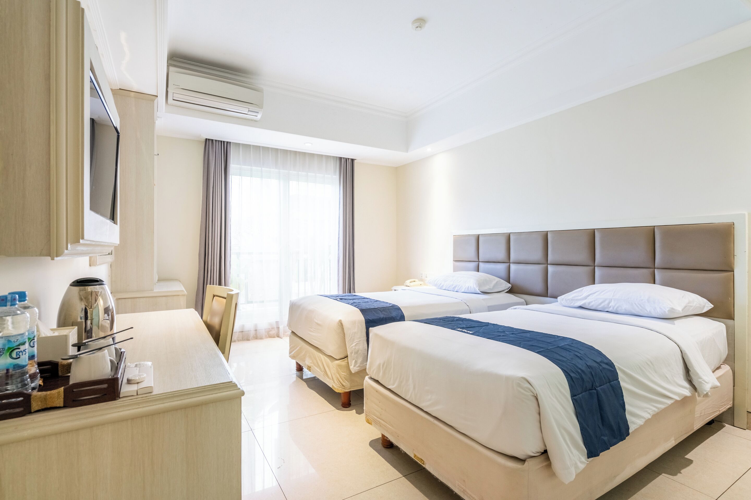 A hotel room with two beds, a desk with a coffee maker, and a TV.