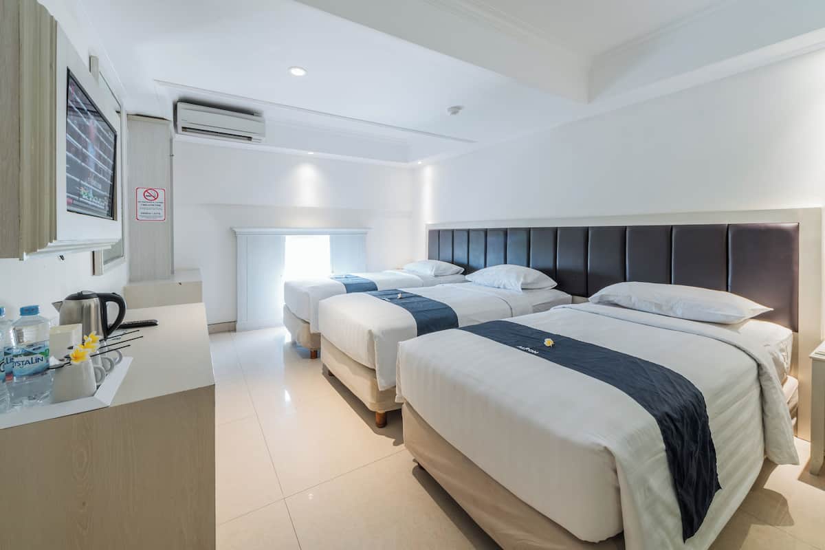 A hotel room with three beds, a desk with a kettle, and a window.