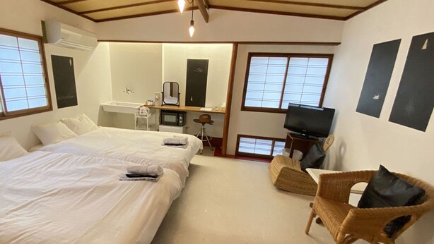 A hotel room with a large bed, a small desk with a chair, a television, and a window with a view. - Guest House Kikusui Ryokan (Tamano)