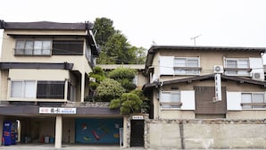 A multi-story building with a ground-level commercial space featuring a vending machine and a colorful mural. - Guest House Kikusui Ryokan (Tamano)