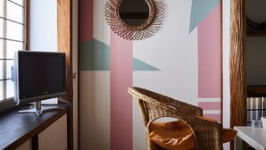 A room with a computer monitor on a desk, a wicker chair, a wall with geometric patterns, and a round mirror. - Guest House Kikusui Ryokan (Tamano)