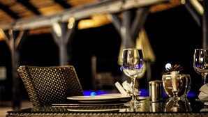 Un tavolo da pranzo apparecchiato con una sedia in vimini, bicchieri da vino, un condimento per sale e un portacandele.