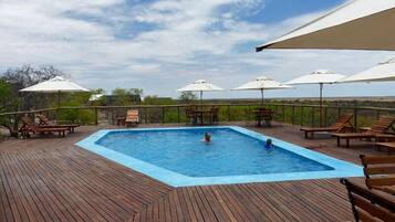 Une piscine rectangulaire sur une terrasse en bois, avec des chaises longues et des parasols.