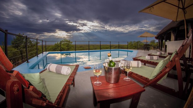 Area piscina con sedie a sdraio, un tavolo con una bottiglia di champagne e calici, e vista sul paesaggio.
