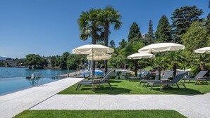 A poolside area with lounge chairs, umbrellas, and a clear view of the water. - Hotel Central am See (Weggis)