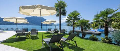 Un espace aménagé au bord de la piscine, avec des chaises longues et des parasols, offrant une vue dégagée sur l’eau et bordé de palmiers.