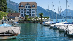 A marina with boats docked, a building with balconies, and mountains in the background. - Hotel Central am See (Weggis)