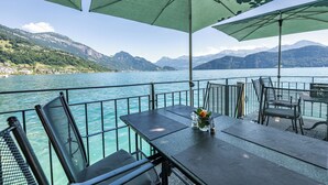 A table with a vase of flowers, outdoor seating with chairs, and a view of a lake with mountains in the background. - Hotel Central am See (Weggis)