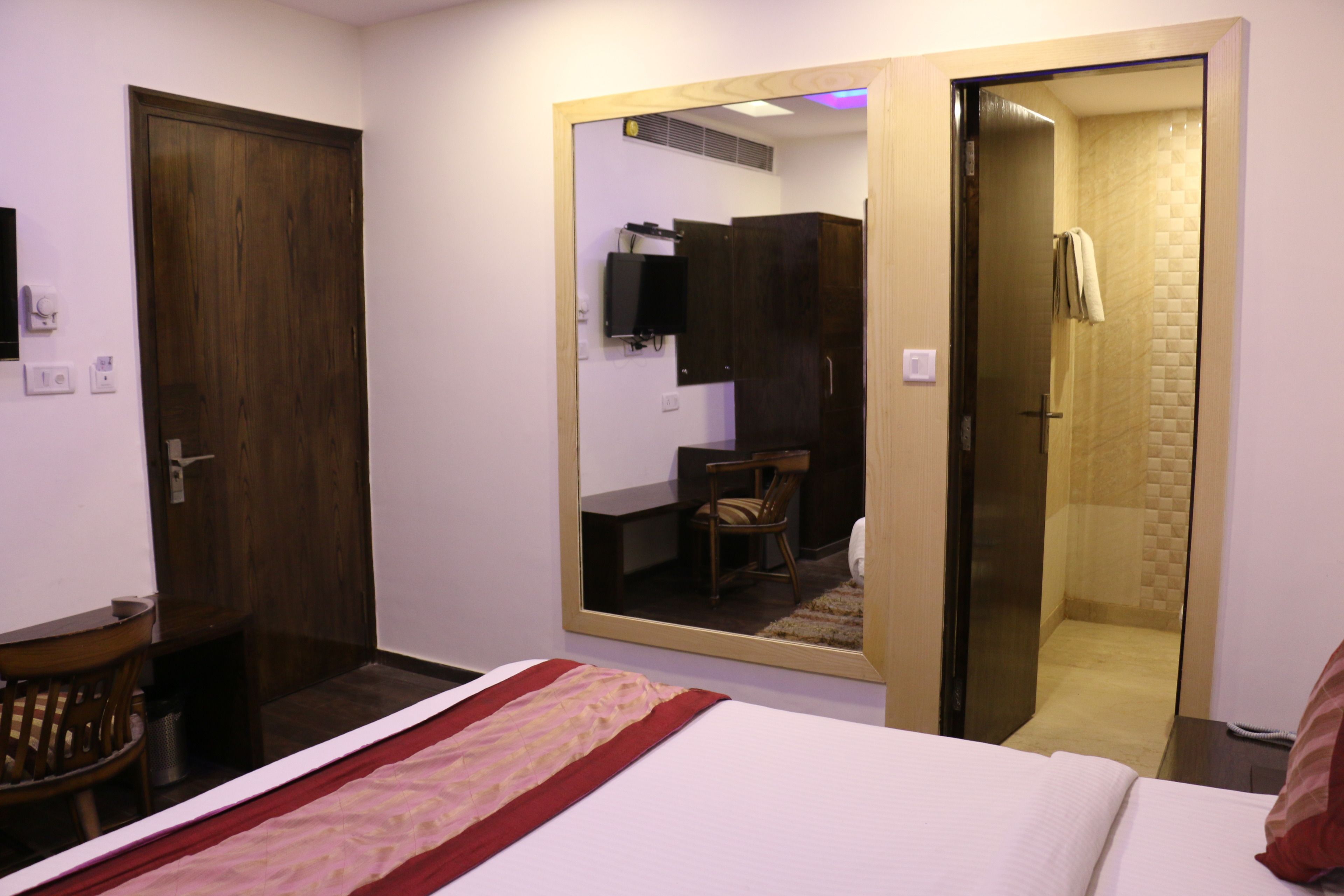 A hotel room with a bed, a mirror, a wooden door, and a shower area.