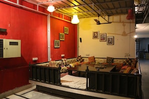A room with a red wall, a sofa with colorful cushions, a table, and a ceiling fan. - Hotel All Iz Well (New Delhi)