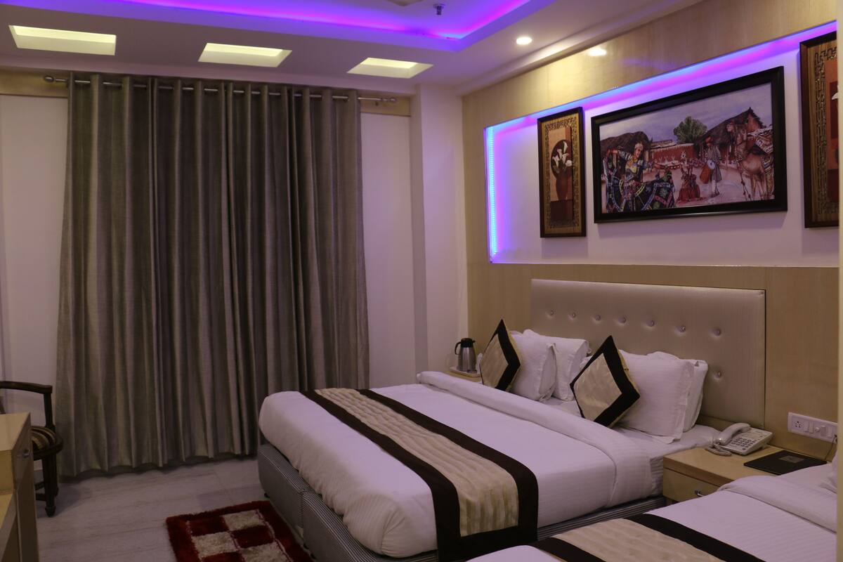 A hotel room with a large bed, a bedside table with a lamp, and a window with curtains.