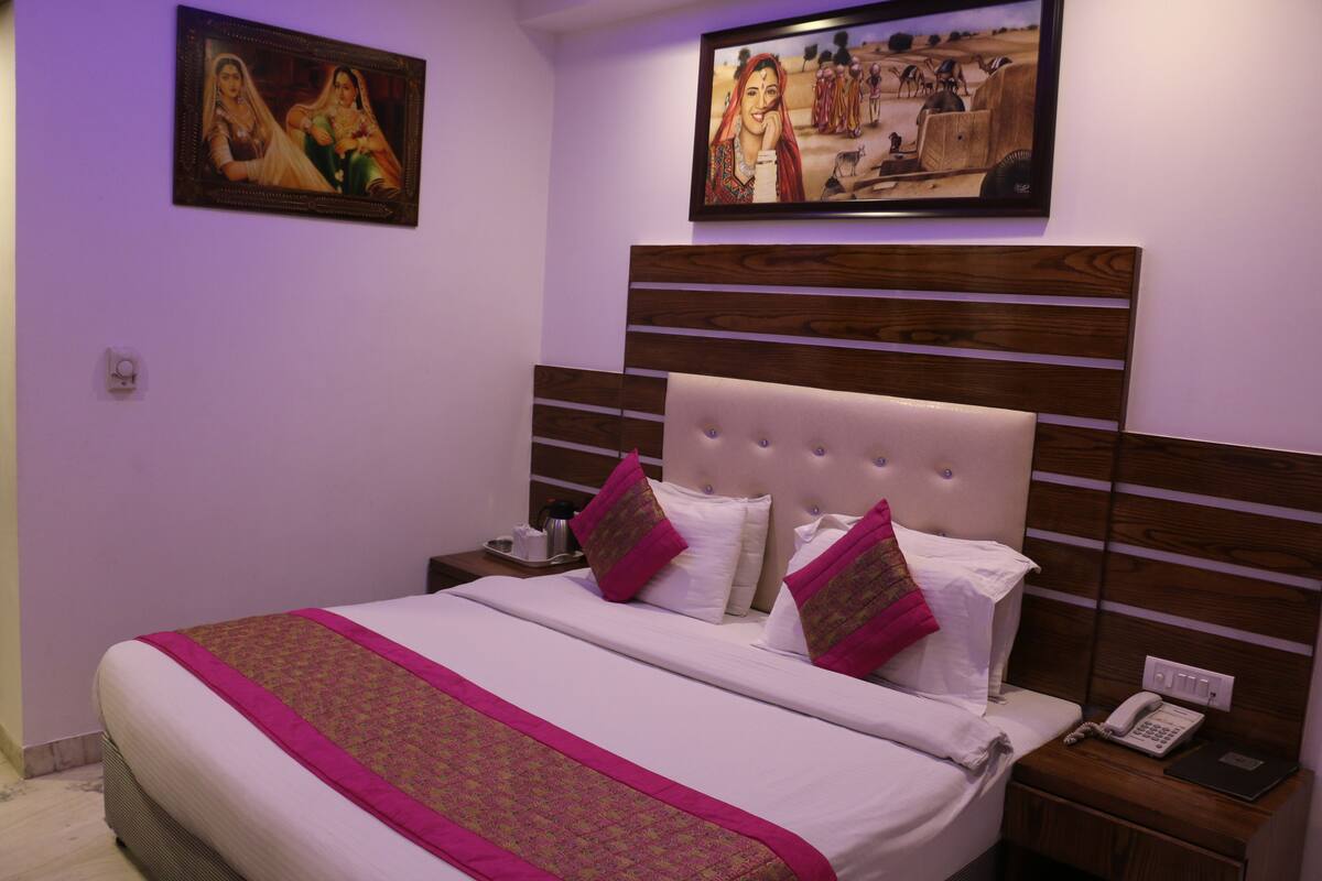 A neatly made bed with a pink and gold bedspread, a wooden headboard, and two bedside tables with a phone and a book.