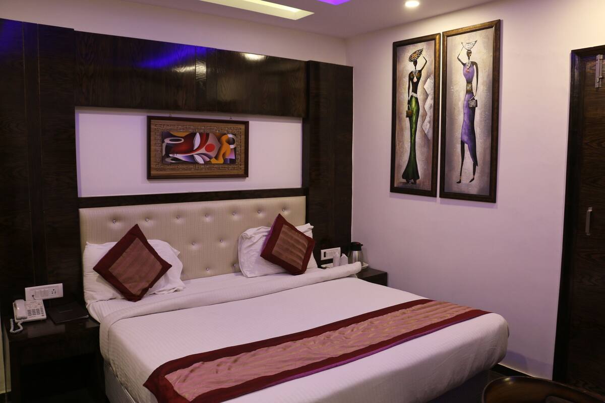 A hotel room with a large bed, a headboard, a bedside table with a phone, and artwork on the walls.