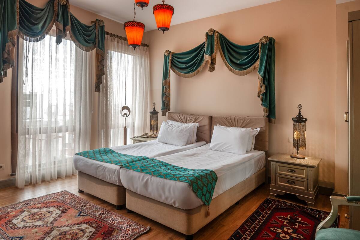 Una cama doble con dos almohadas, una mesita de noche con lámpara y una alfombra estampada.