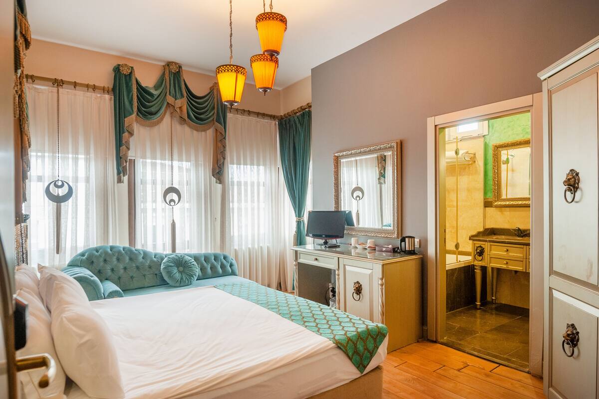 Habitación de hotel con cama, escritorio, computadora y baño visible a través de una puerta abierta.