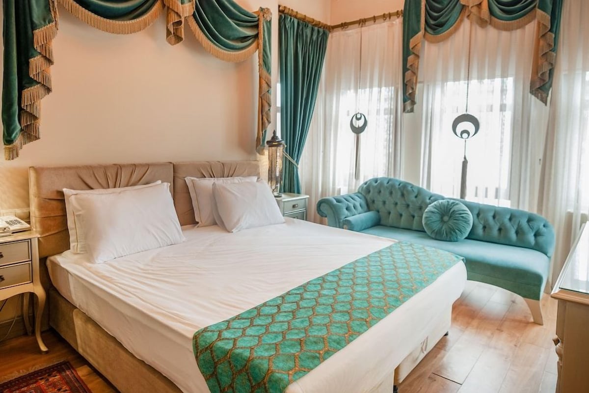 A hotel room with a large bed, a sofa, a nightstand, and curtains.