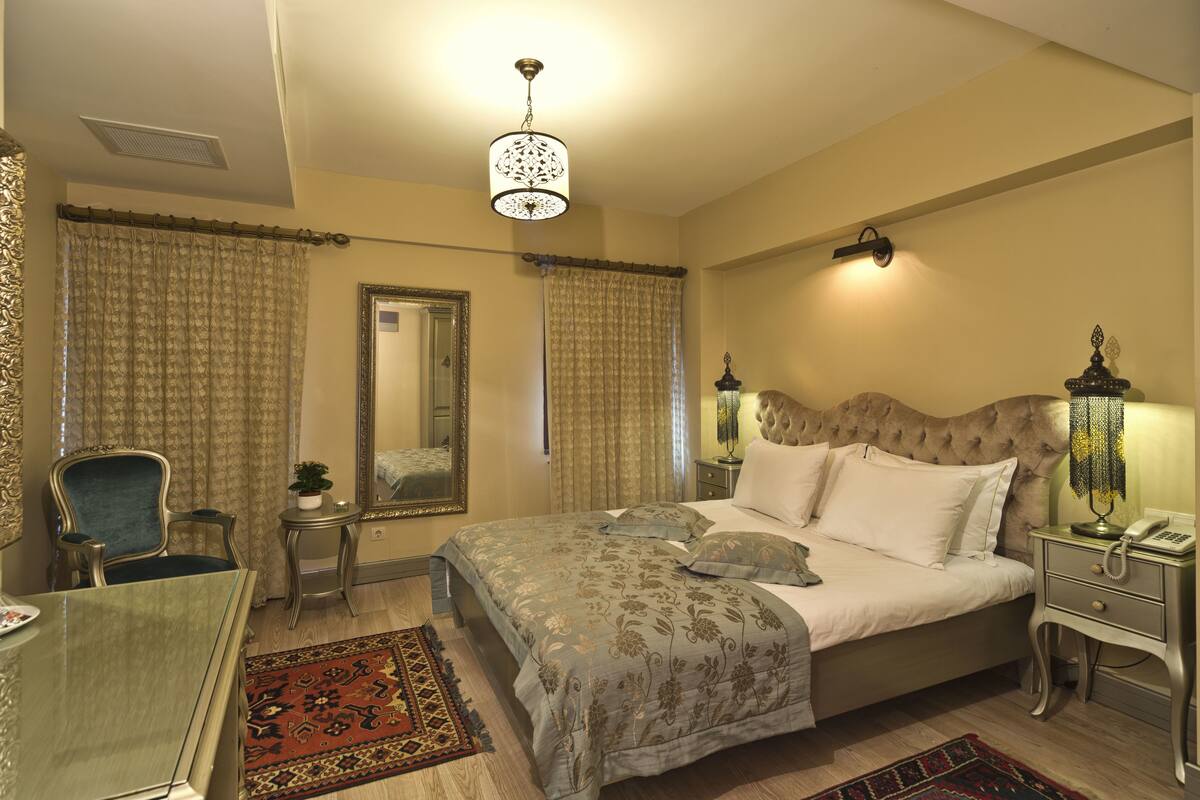 Un dormitorio con una cama grande, una silla, una mesita, un espejo y una lámpara.