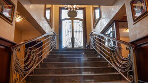 Una imponente escalera con barandillas de metal decoradas y un gran portal ornamental al final.