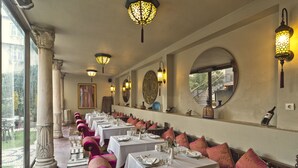 Un amplio comedor con mesas dispuestas para varios comensales, ventanas grandes y apliques decorativos.