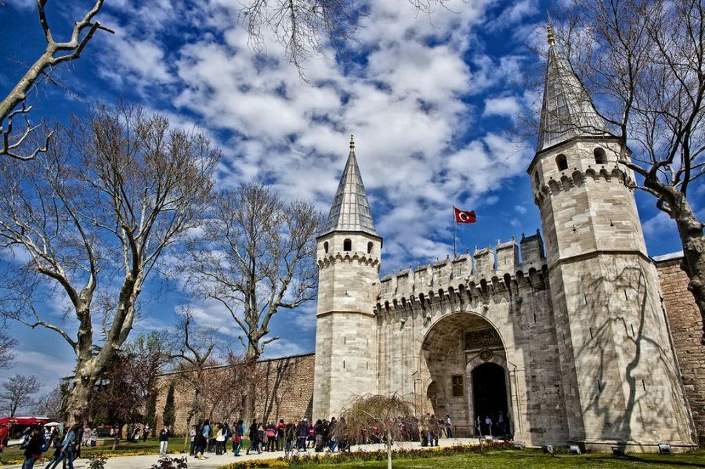 A historic stone gate with a tower, a flag, and leafless trees.